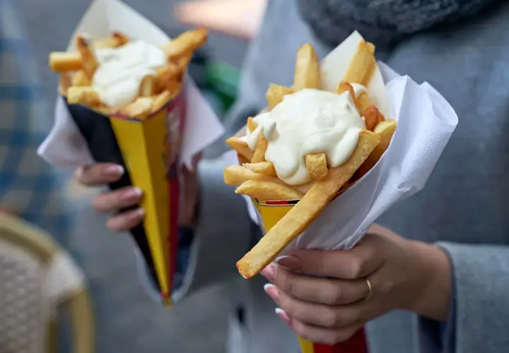 Dwie porcje frytek w papierowych rożkach, polane majonezem.